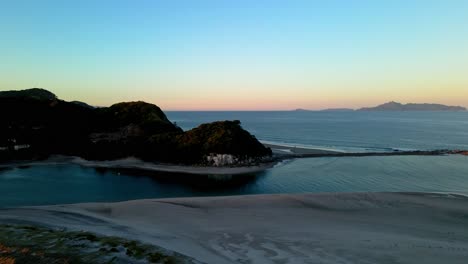Ascending-aerial-shot-showing-silhouette-of-famous-Mangawhai-Heads-during-colorful-sunset-in-New-Zealand
