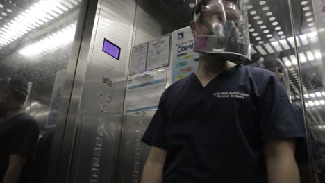 Doctor-Wearing-Respirator-and-Face-Shield,-Pushing-Button-in-Hospital-Elevator