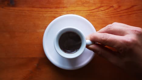 Hand-is-serving-hot-espresso-cup-on-a-white-plate,-standing-on-a-brown-wooden-table