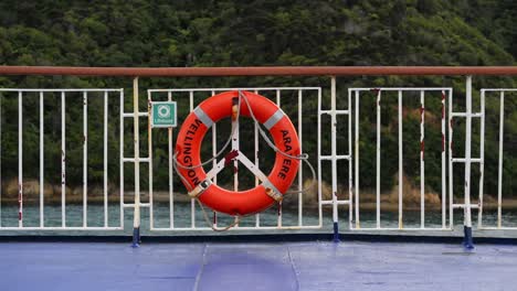 Lifebuoy-on-a-ferry's-railing-with-the-lush-coastal-mountains-of-the-marlborough-sound-in-the-background