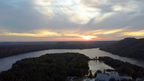 Golden-sunset-over-forest-lake-and-huge-mansion,-aerial-ascend-view