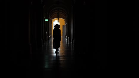Back-View-Woman-Walking-in-Dark-Ancient-Building-Corridor