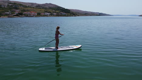 aerial-slow-motion-of-female-tourist-on-paddle-board-in-the-Adriatic-Sea-on-the-coast-of-Pag-Island-on-a-summer-day