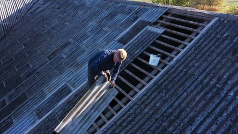 Worker-passing-an-asbestos-slate-for-roof-repairs,-aerial-view