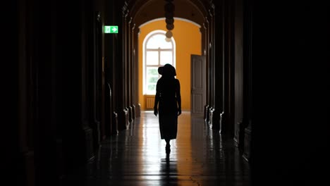 Silhouettierte-Frau,-Die-Im-Dunklen-Korridor-Des-Alten-Barockgebäudes-In-Richtung-Des-Hellen-Gewölbten-Fensters-Geht---Jelgava-palast-Lettland