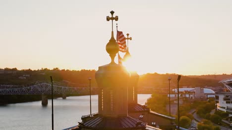 Aerial-view-around-a-US-Flag-waving-in-front-of-the-Ohio-river,-sunset-in-USA---slow-motion,-orbit,-drone-shot