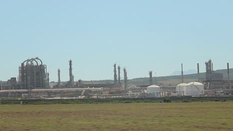 Driving-by-a-gas-and-oil-refinery,-visible-in-the-distance