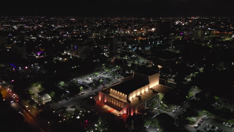 Eduardo-Brito-National-Theater-illuminated-at-night-and-Santo-Domingo-city-in-background,-Dominican-Republic