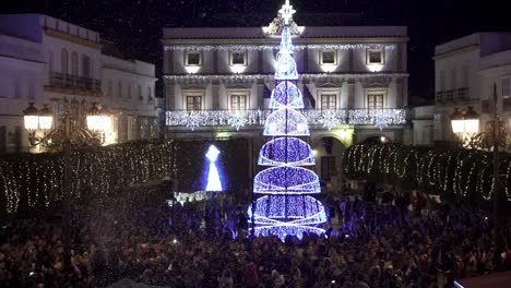 Slow-motion-handheld-shot-of-a-town-square-in-medina-sidonia-in-cadiz-spain-during-a-christmas-festival-with-many-people-in-front-of-a-glowing-blue-christmas-tree-with-star-on-the-top