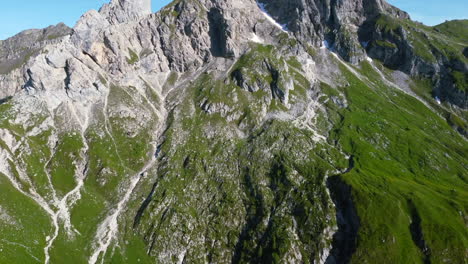 Paisaje-Aéreo-Panorámico-Sobre-El-Pico-De-Los-Dolomitas-En-Un-Día-Soleado-De-Verano-Con-Cielos-Azules-Y-Cara-De-Montaña-Verde-Y-Exuberante