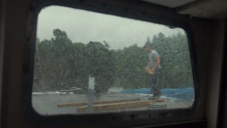 View-through-rainy-boat-window-young-man-puts-on-jacket