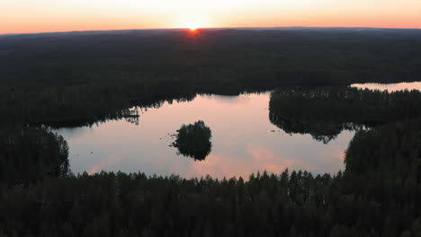 Aerial-drone-circling-point-of-view-shot-of-calm-lake-with-small-island-by-beautiful-sunset-in-the-boreal-wilderness
