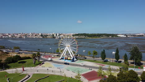 Cars-Driving-On-The-Road-Around-Ferris-Wheel-At-The-City-Park-With-A-View-Of-River-In-Seixal,-Portugal