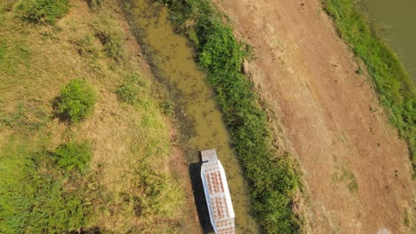An-aerial-hovering-footage-of-a-Boat-Tour-in-Bueng-Boraphet,-Nakhon-Sawan,-Thailand,-as-it-navigates-a-canal-from-the-bottom-going-out-to-the-top-of-the-frame-during-a-summer-day