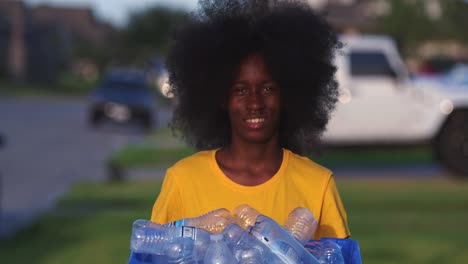 Afroamerikanische-Jugendliche-Mit-Riesigem-Afro-Lächeln,-Während-Er-Den-Papierkorb-Voller-Plastikflaschen-Hält