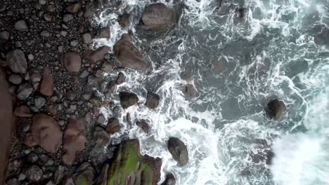 Aerial-of-the-ocean-waves-washing-up-on-rocks-in-black-sand-beach-in-El-Zonte-beach-,-La-Libertad,-El-Salvador