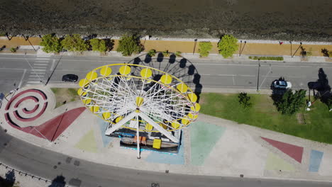 Top-Down-View-Of-Ferris-Wheel-Slowly-Revealing-The-Bay-Of-Seixal---Aerial-shot