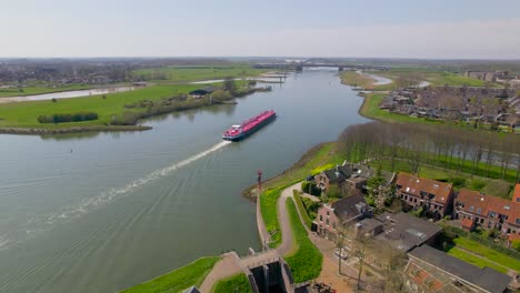 Aerial-view-of-red-boat-sailing-down-river-in-Dutch-countryside