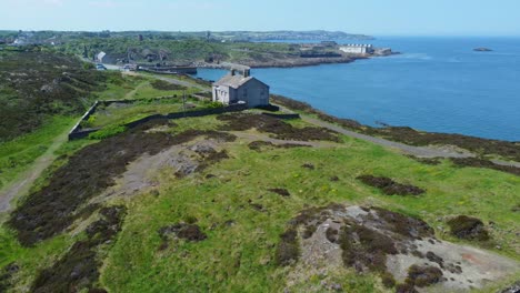 Abandoned-Amlwch-coastal-countryside-mountain-house-aerial-view-overlooking-Anglesey-harbour-pull-back