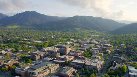 Aerial-shot-of-beautiful-flatiron-mountain-vista-and-bright-green-trees-in-downtown-Boulder-Colorado-during-an-evening-sunset-with-warm-light-on-the-rocky-mountain-town-and-summer-landscape