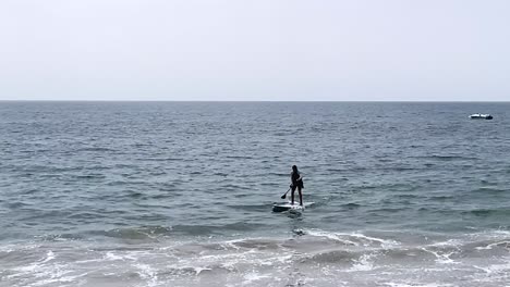 Solo-paddle-boarder-in-the-ocean-paddling-to-the-shore,-Pacific-Coast,-Malibu-California