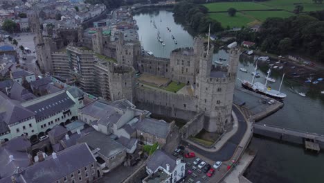 Ancient-Caernarfon-castle-Welsh-harbour-town-aerial-view-medieval-waterfront-landmark-top-down-right-orbit
