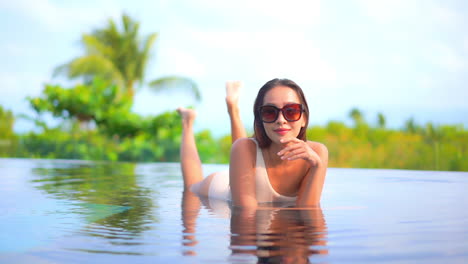 Asiatische-Frau,-Die-Auf-Dem-Bauch-Im-Seichten-Wasser-Des-Schwimmbades-Mit-üppigem-Tropischem-Grün-Im-Hintergrund-Tagsüber-In-Malasia-Liegt