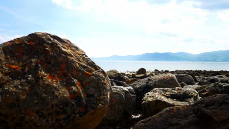 Colourful-variety-of-stone-boulders-beach-landscape-under-North-Wales-mountain-range-lowering-jib-right