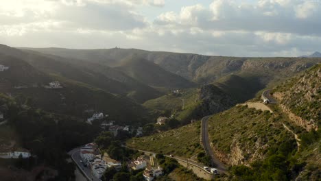 Lange-Luftaufnahme,-Die-Bei-Sonnenuntergang-Rückwärts-Von-Gewundenen-Hügelstraßen-Und-Häusern-Zu-Einer-Wunderschönen-Abgelegenen-Azurblauen-Mediterranen-Bucht-In-Spanien-Fliegt