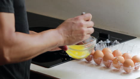 man-beating-eggs-in-a-glass-bowl-near-ceramic-stove-top-in-kitchen