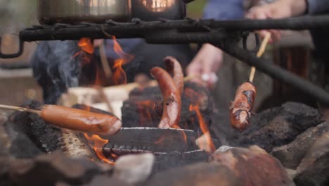 Sausages-on-a-picnic-on-sticks-cooking-in-the-fire-with-tea-pots-made-of-shiny-metal