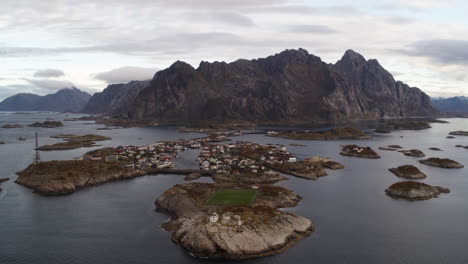 Drone-aerial-view-of-small-village-perched-on-rocky-island-archipelago-at-the-base-of-a-mountain