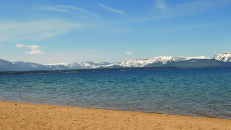 Beautiful-blue-sky-over-Lake-Tahoe-with-an-empty-beach-and-mountains-in-background