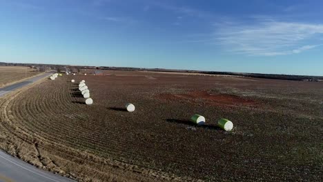 Static-Drone-Aerial-shot-of-a-Midwestern-cotton-farm-with-fresh-bales-of-harvested-cotton-wrapped-in-bright-yellow-material-against-a-blue-open-sky