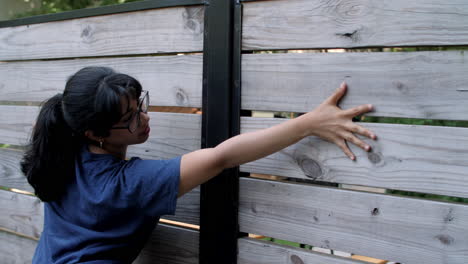 A-young-Latina-woman-wearing-glasses-caresses-a-wood-fence