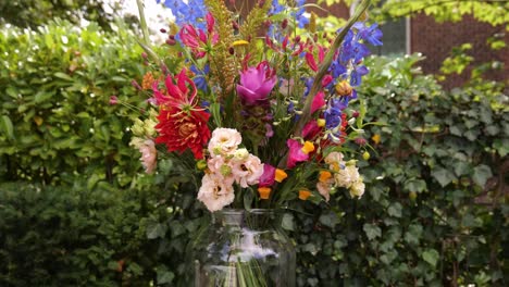 Colourful-Wedding-Flowers-In-Clear-Vase-With-Green-Hedge-In-Background