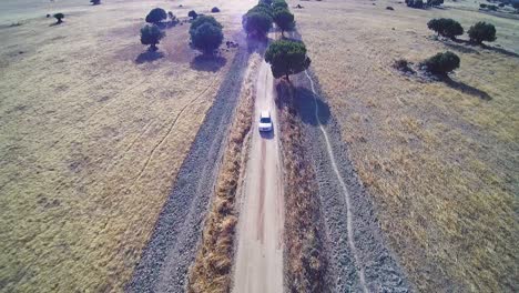 Drone-shot-of-a-silver-car-driving-on-a-dusty-track-in-la-Mancha-in-Spain,-summer-time,-mid-day