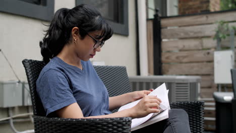 A-young-Latina-woman-sits-on-a-back-patio-studying-a-textbook
