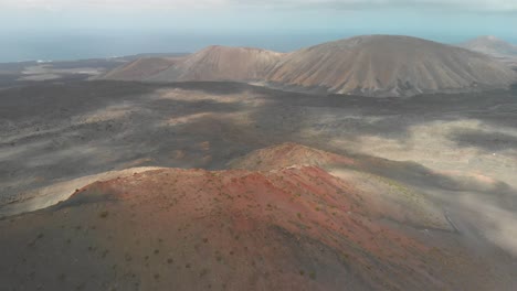 Panning-up-drone-shot-of-a-red-volcano-by-the-ocean-on-a-cloudy-day