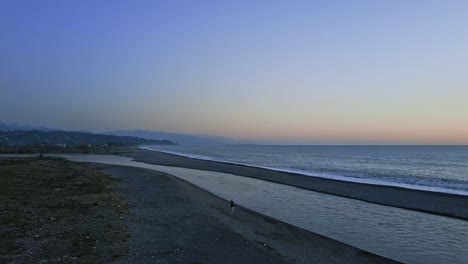Beach-evening-view-with-a-man-running,-sea-with-chill-waves,-deep-blue-sky,-Batumi-in-a-distance