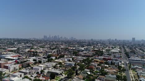 Static-drone-aerial-shot-over-Los-Angeles-neighborhood-with-rooftops,-blue-skies-and-Downtown-LA-in-the-background