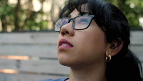 Close-up-of-a-young-Latina-woman-wearing-glasses,-looking-up-to-the-sky-on-a-sunny-day