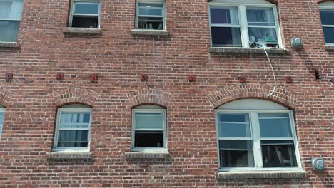Lustige-Nach-Unten-Verfolgende-Drohnenaufnahme-Von-Der-Seite-Eines-Wohnhauses-Aus-Rotem-Backstein-Mit-Fenstern