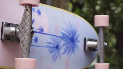Slider-shot-of-skateboard-on-its-side-showing-its-customised-artwork,-pink-wheels