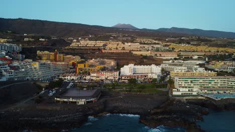 Amazing-Drone-Shot-in-4K-Spain-Tenerife-Los-Gigantes-Island-Volcano-Buildings-Hotels-Mountains-Seaside-Seashore-Water-Sea-Blue-Rocks-Pool