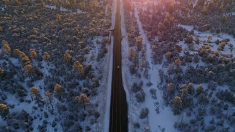 Tracking-aerial-following-car-down-winter-forest-highway-at-sunrise,-4K