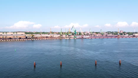 Industrial-cranes-and-buildings-of-Klaipeda-harbor-on-sunny-day,-descending-drone-view