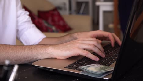 Man-Working-And-Typing-On-Laptop-Computer-With-US-Dollar-Bills