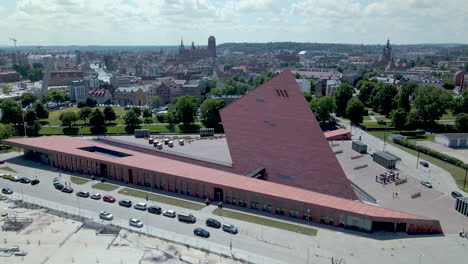 Aerial-drone-shot-of-cars-driving-on-road-beside-modern-second-war-museum-during-summer