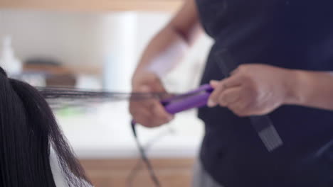 Using-a-hair-straightener-to-on-an-attractive-young-black-teen's-hair-before-styling-it---isolated